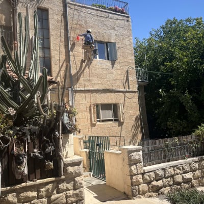 אדם עובד על קיר בניין בגובה עם ציוד בטיחות