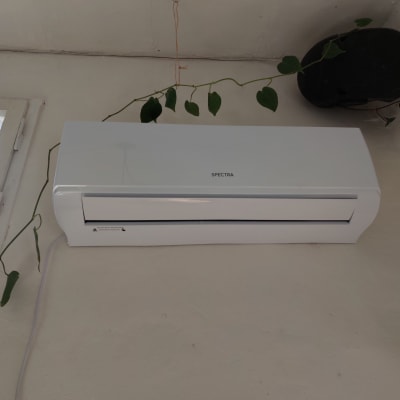 מזגן קיר לבן מותקן על קיר עם צמח מטפס