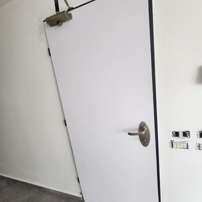 דלת לבנה עם ידית מתכת ומנגנון סגירה עליון