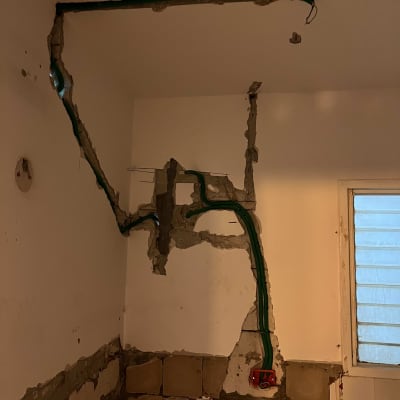 חוטי חשמל ירוקים בקיר חשוף עם שקע אדום