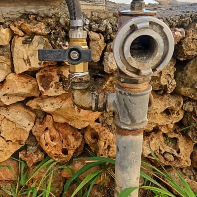 צינור מים עם ברז וחיבורים על רקע קיר אבן