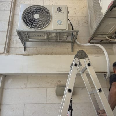 אדם על סולם מתקין מזגן על קיר חיצוני