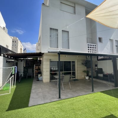 חצר עם דשא סינתטי, שולחן וכיסאות תחת פרגולה