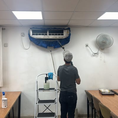 אדם מנקה מזגן עם צינור מים וסולם