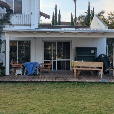 מרפסת עץ עם ריהוט גן ועצים ברקע