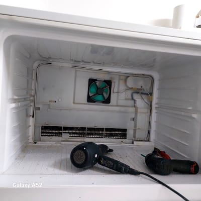 מאוורר ירוק בתוך מקרר פתוח עם כלים לתיקון