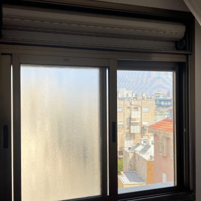 חלון עם תריסים סגורים ונוף עירוני ברקע