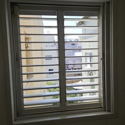 תריסים לבנים על חלון עם נוף עירוני