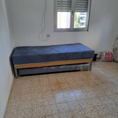 מיטה עם מזרן כחול ליד חלון עם תריסים