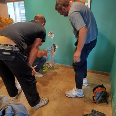 שני אנשים עובדים על קיר עם כלי עבודה, חוטי חשמל וכלים נוספים