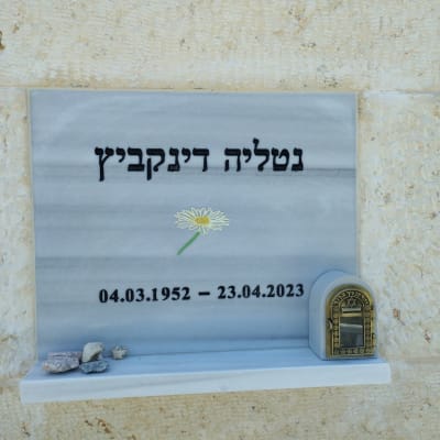 מצבה עם כיתוב בעברית, פרח ואבנים קטנות