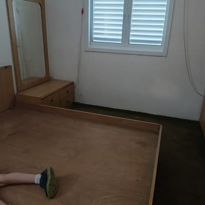 חדר ריק עם מיטה ללא מזרן, חלון עם תריסים