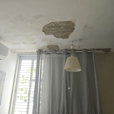 תקרה עם קילופי צבע ונזקי רטיבות ליד חלון ווילון