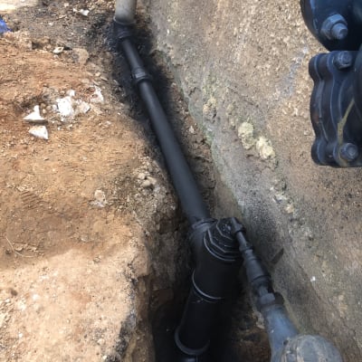 צינור ביוב שחור מותקן באדמה ליד קיר בטון