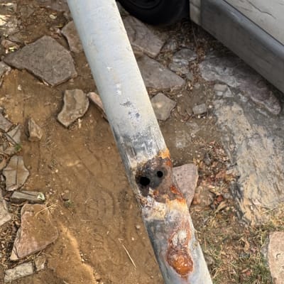 צינור חלוד עם חורים על רקע קרקע ואבנים