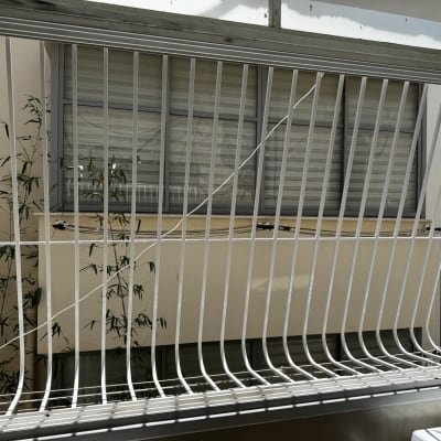 סורגי מתכת לבנים על חלון עם צמחי במבוק ברקע