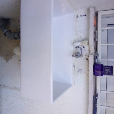 כיור לבן עם ברז וצינורות על קיר חיצוני