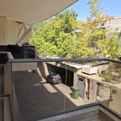 מעקה זכוכית במרפסת עם נוף לעצים וחצר