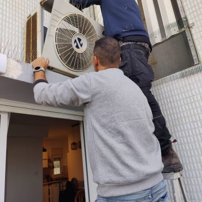 שני אנשים מתקינים מזגן חיצוני על קיר בניין