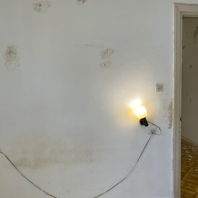 קיר עם תיקוני טיח וכתמי צבע, מנורה מחוברת לשקע