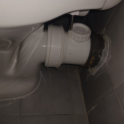 חיבור צינור לבן לאסלה על רקע אריחים אפורים