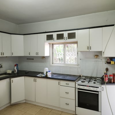 מטבח עם ארונות לבנים, כיריים וגז, חלון עם סורגים