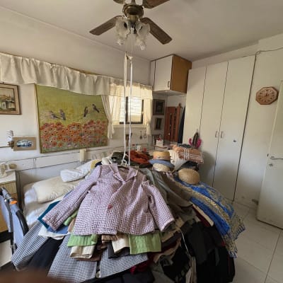 חדר עם בגדים על המיטה, טלפון שולחני, ציור על הקיר