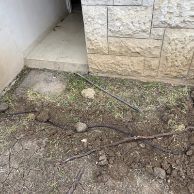 כבל שחור מונח על אדמה ליד קיר אבן