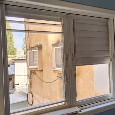 תריסים לבנים פתוחים וחלקית סגורים בחלון