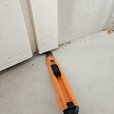 סכין חיתוך כתום ליד דלת לבנה על רצפה אפורה