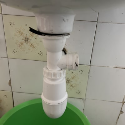 צינור ניקוז לבן מתחת לכיור עם דלי ירוק