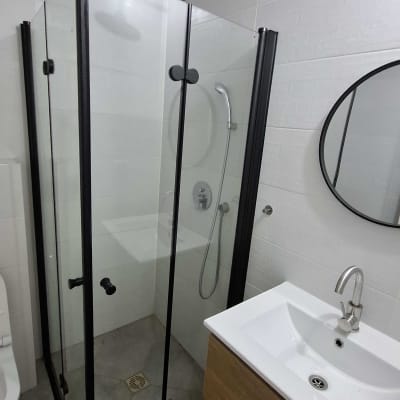 מקלחון זכוכית עם ראש מקלחת עגול וכיור בחדר אמבטיה