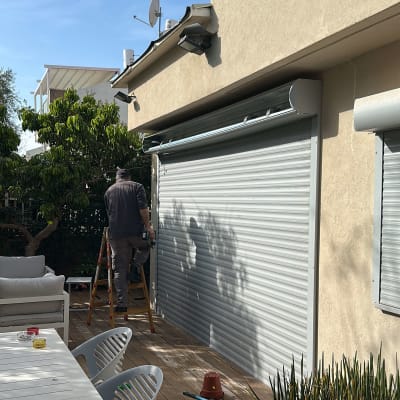 אדם מתקין תריסים חיצוניים על קיר בית
