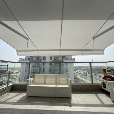 מרפסת עם סוכך לבן מעל ספה וריהוט חוץ