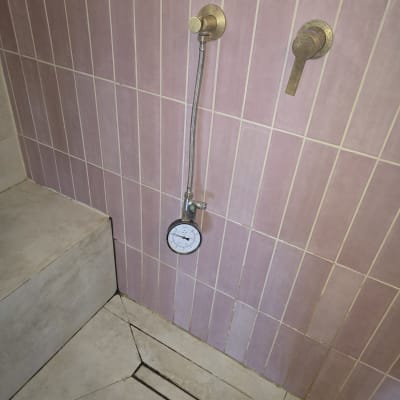 מד לחץ מים מחובר לקיר אריחים ורודים במקלחת