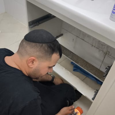 אדם עובד מתחת לכיור עם כלי עבודה