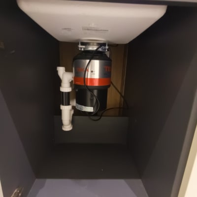 כיור עם טוחן אשפה וצנרת מתחת לארון