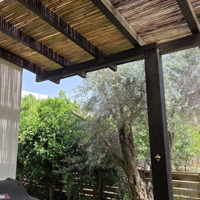 פרגולה מעץ בגינה עם דק ועצים ברקע