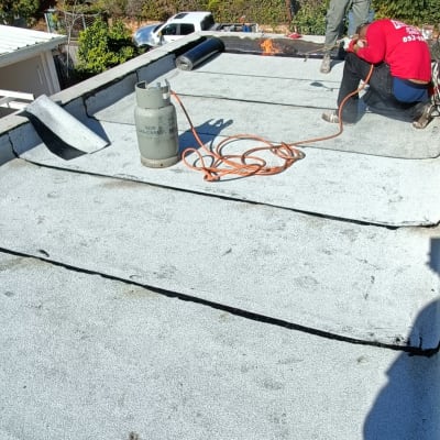 עובדים אוטמים גג עם יריעות ביטומניות ומבער גז