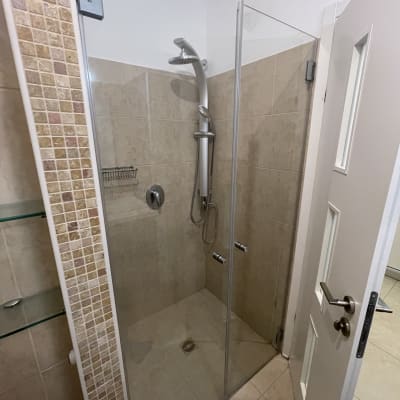 מקלחת נקייה עם דלת זכוכית וראש מקלחת כסוף