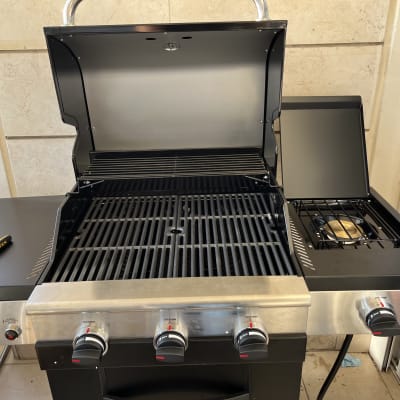 גריל גז עם כיריים צדדיות וכלי עבודה על שולחן.