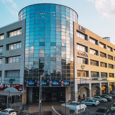 בניין עם חזית זכוכית, מכוניות חונות, שמיים מעוננים