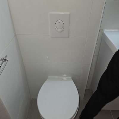 אסלה לבנה עם לחצן הדחה על קיר אריחים לבנים