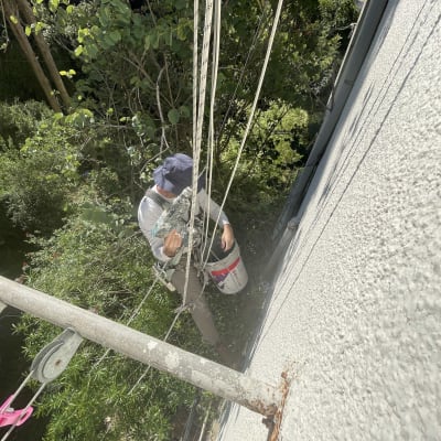 אדם מבצע עבודות גובה על קיר חיצוני עם דלי צבע