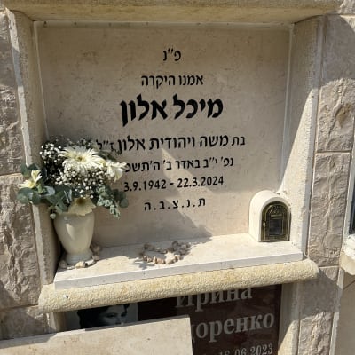 מצבה עם כיתוב בעברית, פרחים ואבנים קטנות