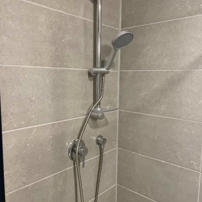 ראש מקלחת עם צינור מתכת על קיר אריחים