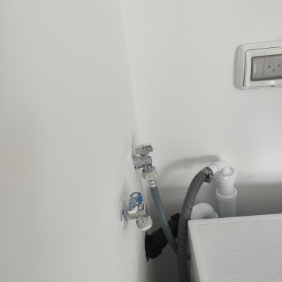 ברזים וצינורות מחוברים לקיר ליד מכונת כביסה