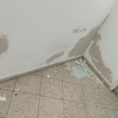 קיר עם תיקוני טיח וקליפות צבע מתקלפות על הרצפה