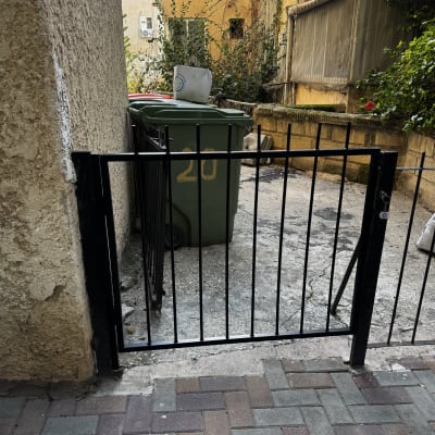 שער מתכת קטן ליד פח אשפה בחצר