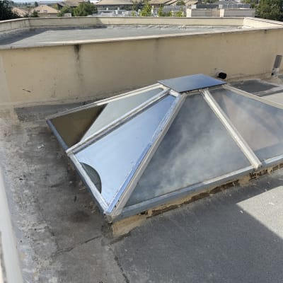 חלון זכוכית משופע על גג שטוח עם מסגרת מתכת.